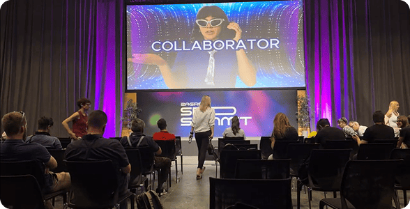 Члени конференції в Загребі, що сидять на стільцях і дивляться на великий екран, на якому транслюється промо-відео Collaborator.